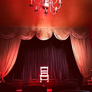 Bühne im leeren Galli Theater, ein einzelner beleuchteter Stuhl vor rotem Vorhang
